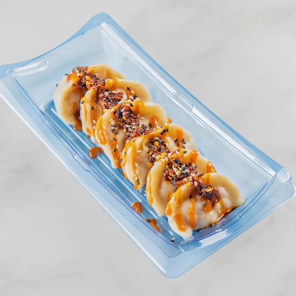 Bun Buds dumplings in a blue plastic container, drizzled with orange sauce and chili flakes.
