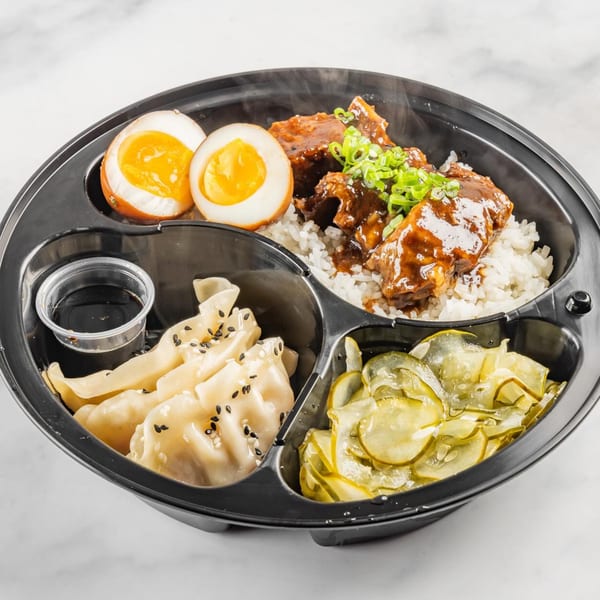 A Bun Buds bento box with rice, braised pork, soft-boiled eggs, dumplings, and pickled cucumbers.
