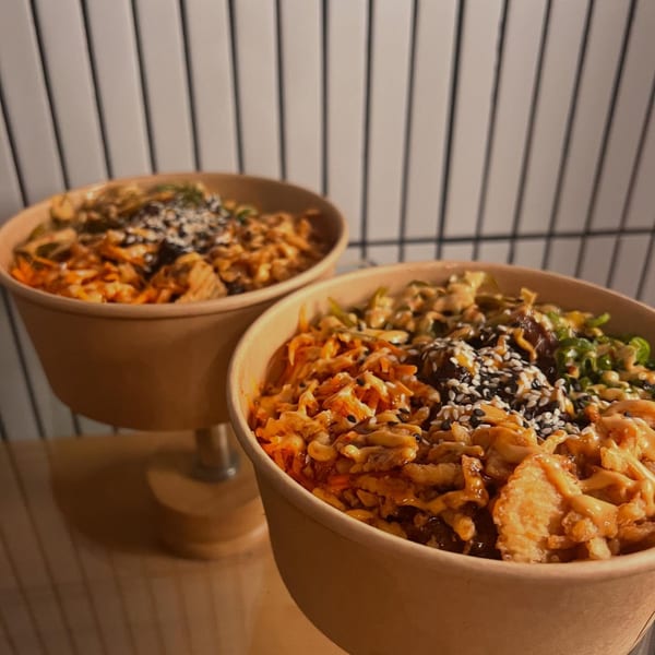 Two Bun Buds fast-food bowls filled with various toppings, sauces, and sesame seeds.