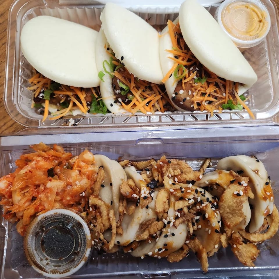 Two clear plastic containers of Bun Buds fast-food, with bao buns, kimchi, and dumplings.