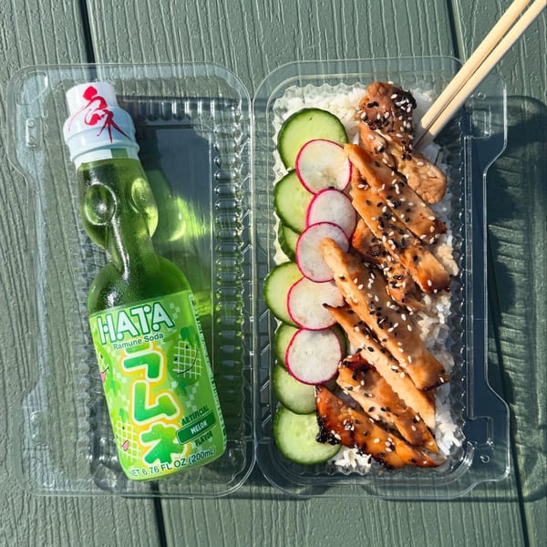Teriyaki chicken with rice, cucumbers, radishes, and a green HATA Ramune soda in plastic containers.
