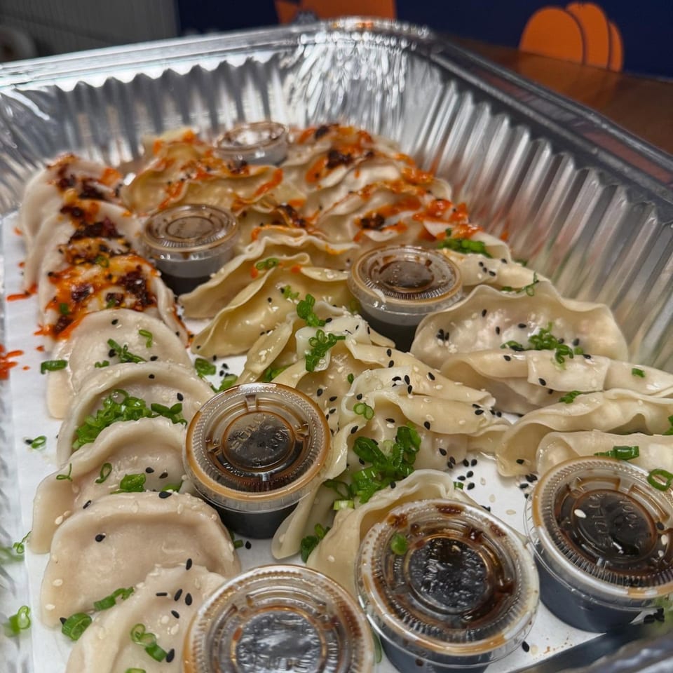 Bun Buds' dumplings in a foil tray, some with chili oil, others with sesame seeds and scallions.