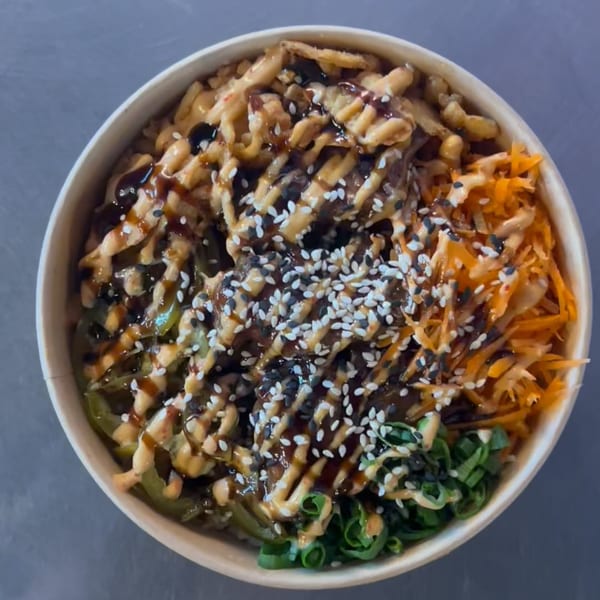 Top-down view of a Bun Buds fast-food bowl with noodles, vegetables, sauces, and sesame seeds.