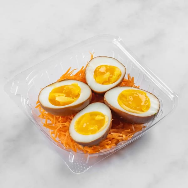 Four halved tea eggs with rich orange yolks, served on shredded carrots in a clear plastic container.