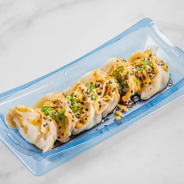 Five Bun Buds dumplings in a blue tray, topped with sauce, sesame seeds, and green onions.
