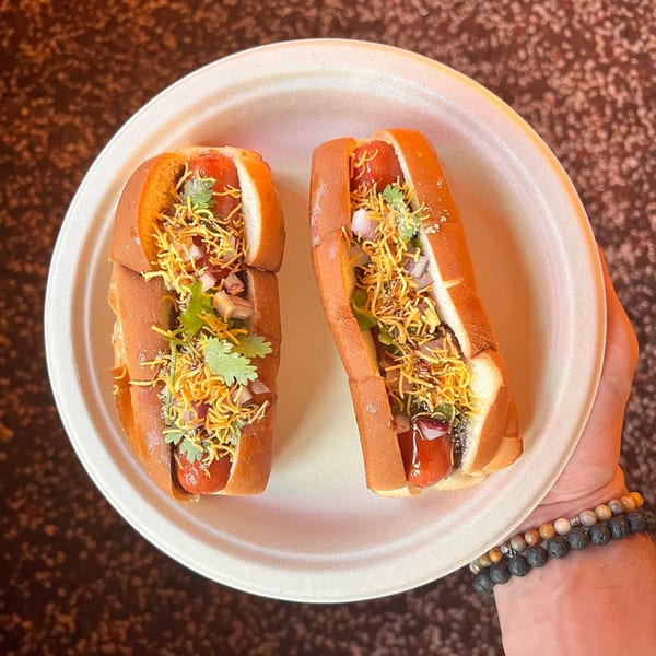 Two Bun Buds hot dogs with toppings, held on a white plate by a person's hand.