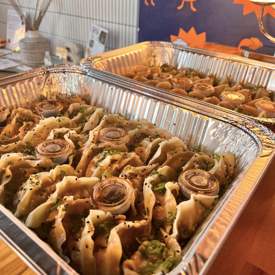 Two foil trays filled with Bun Buds dumplings, topped with sesame seeds, green onions, and sauce cups.
